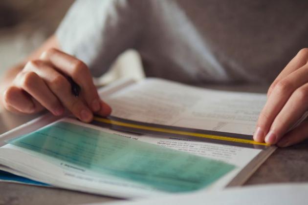 Persona che studia con un righello e un foglio trasparente su un libro.