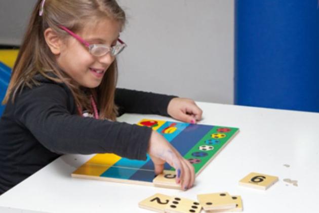 Bambina con occhiali gioca con puzzle educativo su un tavolo bianco.